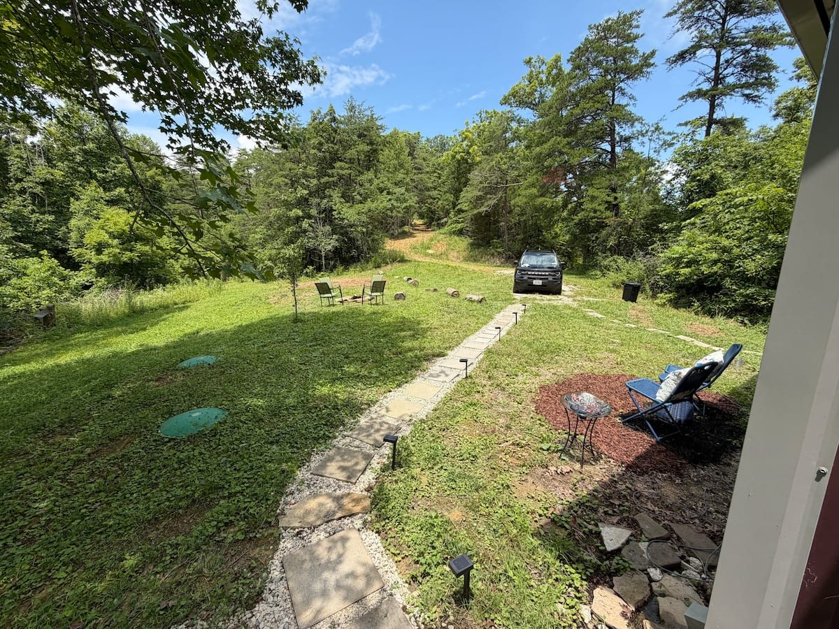 Stone fire pit and chairs in a grassy clearing by the woods